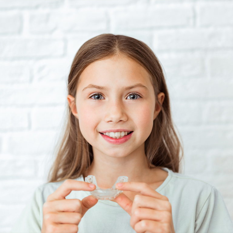 Young Smiling Girl Holding Invisalign Aligner